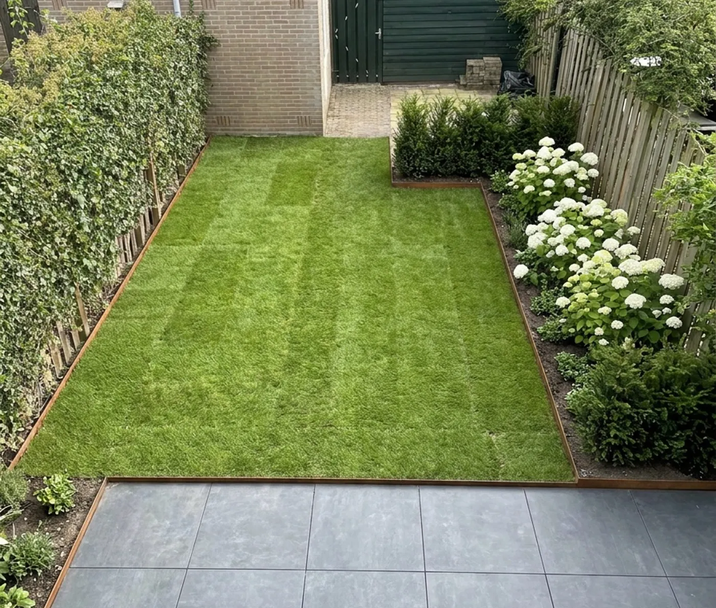 De achtertuin na de aanleg: terras, gazon met cortenstaal rand en hortensia's